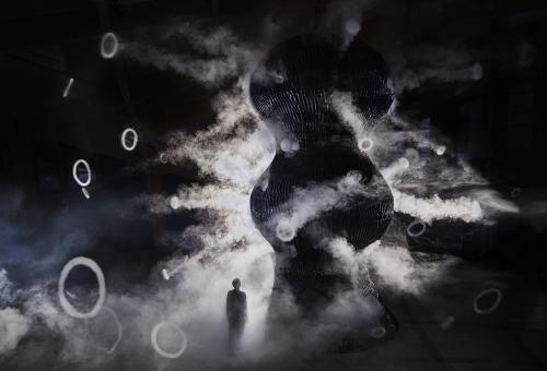 A view of the infinity blue sculpture it's a dark image with a ray of light coming from the left hand side showing a figure standing and looking up at the large sculpture